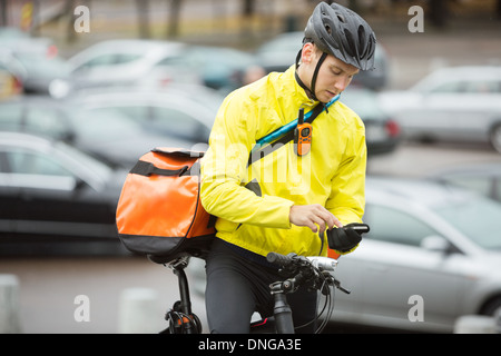 Männliche Radfahrer mit Kuriertasche mit Handy auf Straße Stockfoto