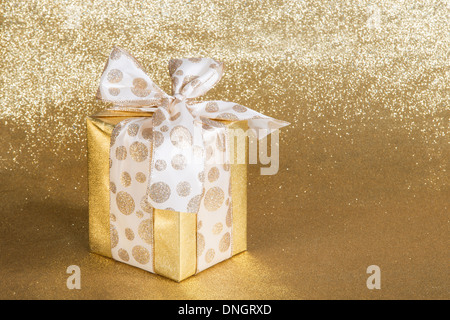 Goldenen Geschenk verpackt mit gepunkteten Schleife über glitzernden goldenen Hintergrund Stockfoto