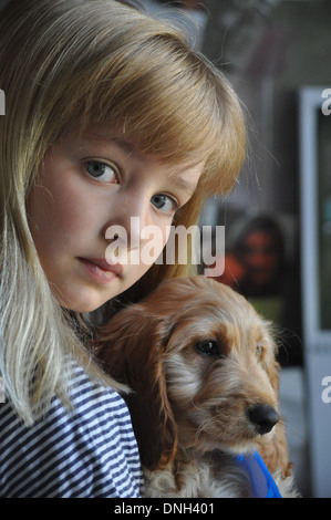 Kleine blonde Mädchen wirkt nachdenklich, als sie ihre neue Cockapoo Pudel Welpen Hund umarmt Stockfoto