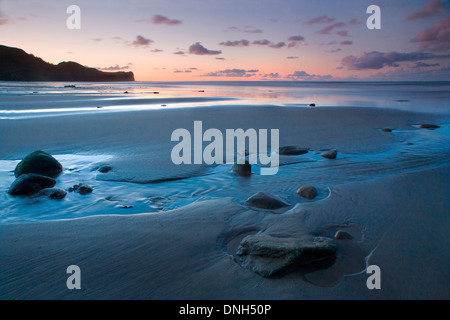 Die zurückweichenden Flut lässt einen Pool um eine Gruppe von Felsen im Sand am Strand von Whitbys, North Yorkshire bei Sonnenuntergang. Stockfoto