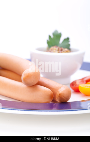 Drei kalt geräucherte Würstchen oder Wiener Würstchen serviert auf einem Teller mit einem Sprung in eine kleine Schüssel geben und in Scheiben geschnittenen Kirschtomaten auf ein weißes Studio-Hintergrund Stockfoto