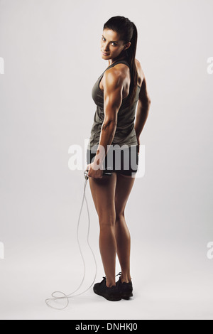 Vertikale Aufnahme des jungen weiblichen Übungen mit einem Springseil über Schulter in die Kamera schaut. Muskulöse Frau Ausübung Stockfoto