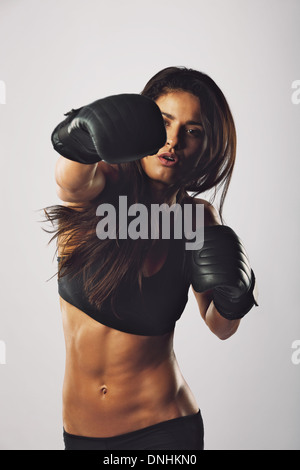 Passen Sie junge Frau trägt Boxhandschuhe Stanzen in Richtung Kamera vor grauem Hintergrund. Hispanische Boxerin Boxen üben. Stockfoto