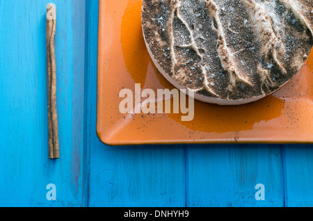 Tiramisu-Kuchen auf eine orange Platte über einen rustikalen Holztisch. Zimtstange Stockfoto