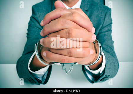 ein Mann in einem Anzug sitzt in einem Schreibtisch mit Handschellen in seine Handgelenke Stockfoto