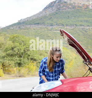 Junge Frau in der Nähe von kaputten Auto braucht Hilfe suchen unter geöffneter Haube Stockfoto