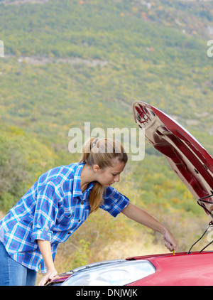 Junge Frau in der Nähe von kaputten Auto braucht Hilfe suchen unter geöffneter Haube Stockfoto