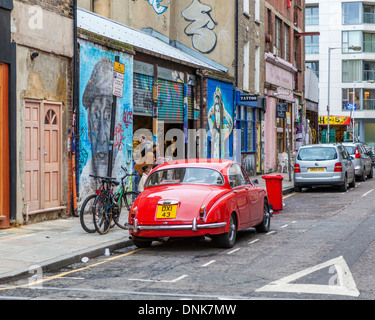 Geparkten roten Oldtimer, Charlie Burns Street Art und second-hand-Möbelgeschäfte in Speck Straße aus Ziegelstein-Weg, East London, UK Stockfoto