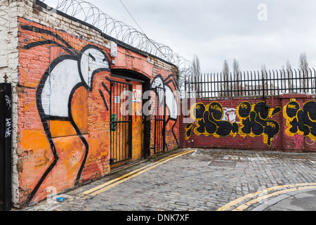 Urban Street Art - schwarz, weiß und orange Strichmännchen und Tags in Grimsby Street, aus Ziegelstein-Weg, East London, UK Stockfoto