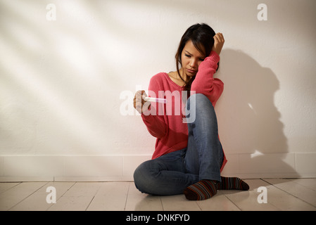Frauen und Gesundheit, ängstlich Asiatin Blick auf Schwangerschaft Test-Kit, auf Boden zu Hause sitzen Stockfoto