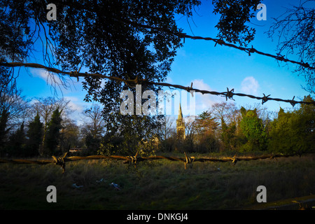 Auf der Suche durch Stacheldraht über immergrüne Feld aus Wanstead Hauptstraße. Der Turm der Christuskirche ist im Hintergrund. Stockfoto