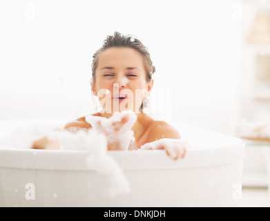 Glückliche junge Frau spielt mit Schaum in der Badewanne Stockfoto