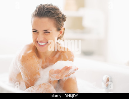 Porträt der glückliche junge Frau spielt mit Schaum in der Badewanne Stockfoto