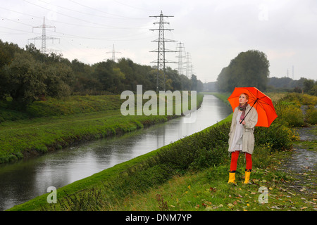 Oberhausen, Deutschland, geht eine junge Frau im Regen mit Regenschirm zu Fuß entlang der Emscher Stockfoto