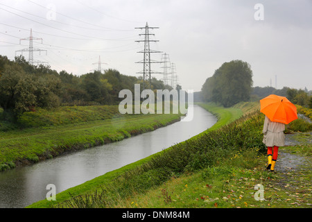 Oberhausen, Deutschland, geht eine junge Frau im Regen mit Regenschirm zu Fuß entlang der Emscher Stockfoto