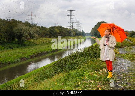 Oberhausen, Deutschland, geht eine junge Frau im Regen mit Regenschirm zu Fuß entlang der Emscher Stockfoto