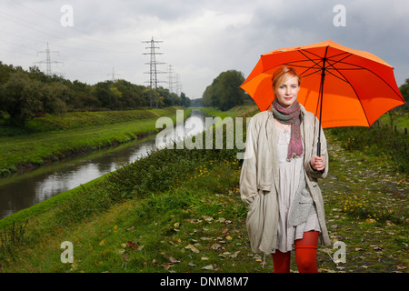 Oberhausen, Deutschland, geht eine junge Frau im Regen mit Regenschirm zu Fuß entlang der Emscher Stockfoto