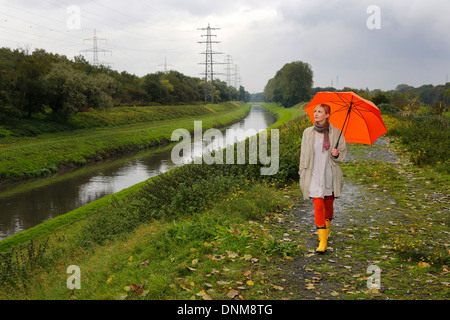 Oberhausen, Deutschland, geht eine junge Frau im Regen mit Regenschirm zu Fuß entlang der Emscher