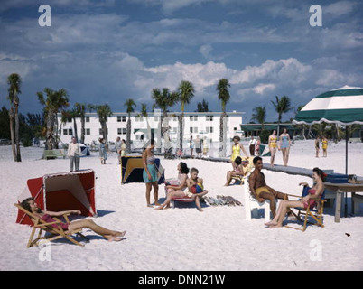 Sonnenanbeter genießen einen Tag am Lido Beach am Lido Key im Sarasota County, Florida, während der 1950er Jahre Das Foto zeigt Einzelpersonen, die sich in Badeanzügen auf dem Sand entspannen, mit Palmen und Strandgebäuden im Hintergrund, die die Strandkultur aus der Mitte des 20. Jahrhunderts widerspiegeln. Stockfoto