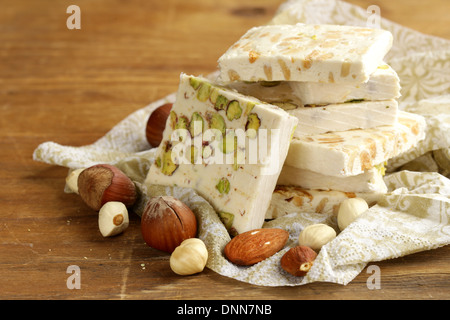 weißer Nougat mit verschiedenen Nüssen auf einem Holztisch Stockfoto