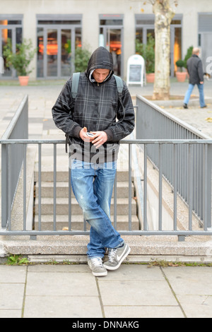 Kaukasische junge Mann mit Kapuzen Jacke Winterkleidung mit seinem Smartphone an einem öffentlichen Ort Stockfoto