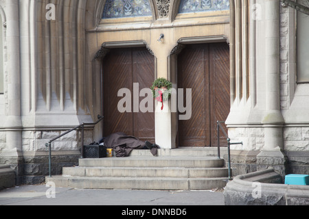 Homelessman schläft auf der Türschwelle einer Kirche an der 7th Avenue in Park Slope, Brooklyn, NY. Stockfoto