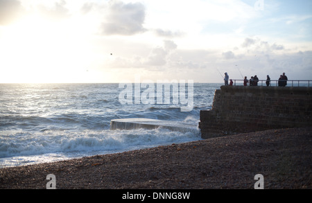 Wellen angespült am Strand von Brighton als Männer Fische an einem Steg / Stein Pier bei Sonnenuntergang am Weihnachtstag Stockfoto