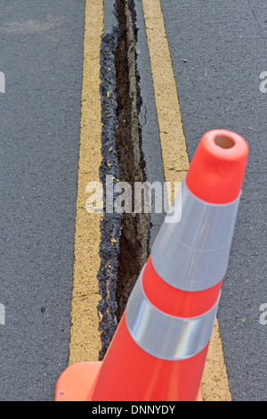 Nahaufnahme von einem orangefarbenen Kegel mit einem großen Asphalt Riss in der Straße hinter sich Stockfoto