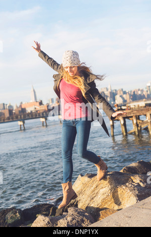 USA, New York City, Brooklyn, Williamsburg, blonde Frau, die auf Steinen Fluss, Skyline im Hintergrund treten Stockfoto