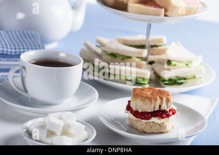 Tasse Tee mit Würfelzucker und Scones, Gurken sandwiches im Hintergrund Stockfoto