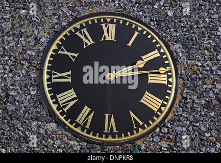 Runde schwarze Uhr mit goldenen römischen Ziffern an der Feuerstein-Wand befestigt Stockfoto