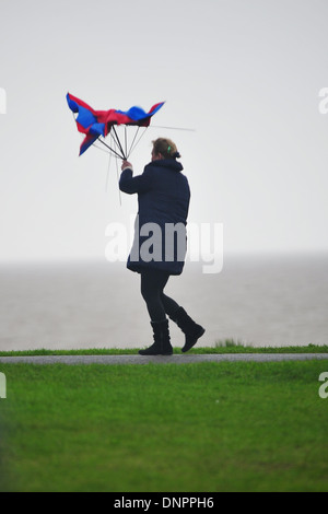 Eine Frau kämpft gegen den Wind mit einem Regenschirm in Barry Island, Wales, Großbritannien. Stockfoto