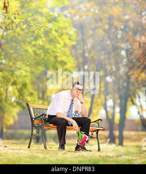 Trauriger junger Mann hält einen Blumenstrauß und sitzen auf einer Bank in einem park Stockfoto