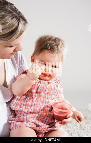 Porträt von Baby Girl Fütterung selbst auf Mutters Schoß, Studioaufnahme Stockfoto