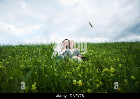 Älteres Paar sitzt im Bereich des Grases, umarmen, Deutschland Stockfoto