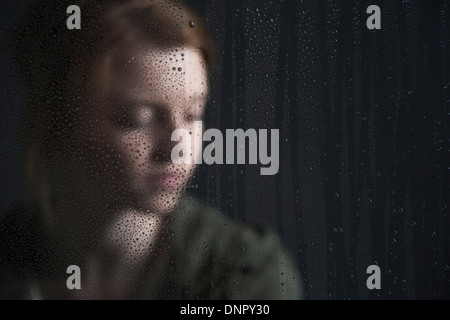 Porträt von Teenager-Mädchen hinter Fenster, nass mit Regentropfen Stockfoto