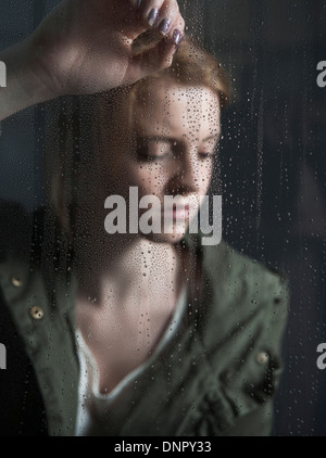 Porträt des Mädchens nass mit Regentropfen-Fenster gelehnt Stockfoto