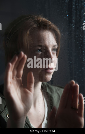 Teenager-Mädchen auf der Suche mit den Händen auf Fenster, nass mit Regentropfen Stockfoto