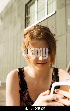 Teenager-Mädchen im Freien zu sitzen und mit Blick auf smartphone Stockfoto