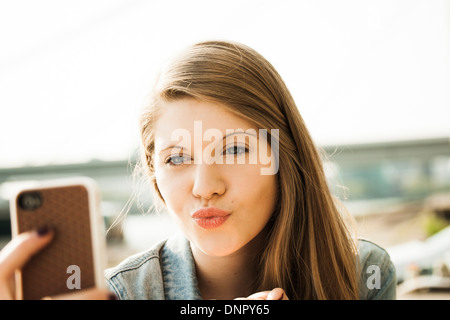 Junge Frau im freien spitzte Lippen beim Smartphone betrachten Stockfoto