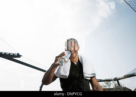 Reifer Mann mit Handtuch um den Hals, Flasche Wasser trinken und Blick in die Kamera, Deutschland Stockfoto
