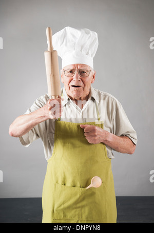 Älterer Mann mit Schürze und Küchenchefs Hut mit Nudelholz in Studio Stockfoto