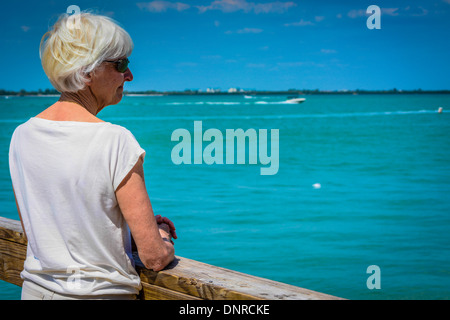 Blick über die Schulter eine ältere weiße Frau alleine wie sie über Meer vom Pier blickt Stockfoto