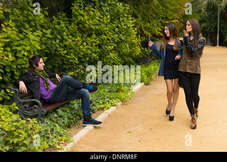Junge Frauen flirten mit einem Mann auf einer Parkbank Stockfoto