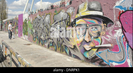 Künstler malen lila Farbe auf einem Abschnitt der Graffiti mit Männerkopf mit Hut, Brille, Zigarette, innere Mauer, Mauerpark Stockfoto