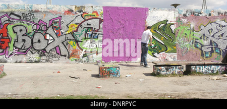 Künstler mit einer Walze-Bürste mit lila Farbe über einen Abschnitt des Graffiti Gekritzel auf innere Mauer, Mauerpark malen Stockfoto