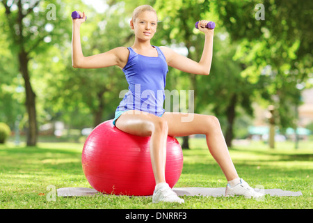 Blonde Sportlerin im Park sitzen auf einem Ball Pilates und Training mit Hanteln Stockfoto