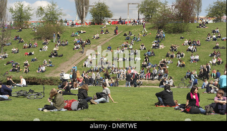 Blauer Himmel weiße Wolken Ansicht Leute sitzen entspannend Grashang unter Berliner Mauer Grenze Streifen Innenwand, Mauerpark, Berlin Stockfoto