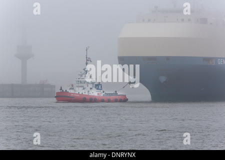 Ein Schlepper mit einem Frachter im Hamburger Hafen mit Nebel, Deutschland Stockfoto