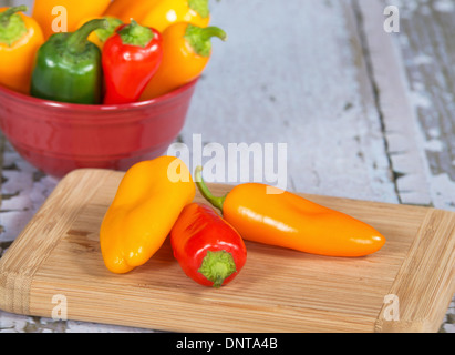 Bunte Mini-Paprika auf Schneidebrett. Eine Schüssel mit sortierten Paprika auf dem Hintergrund. Stockfoto